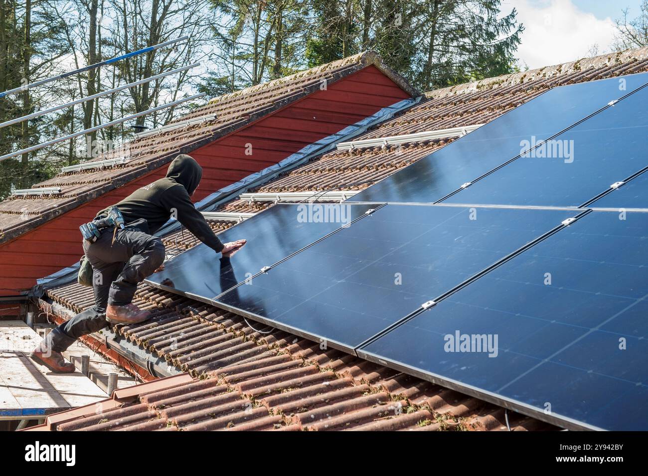 Ein Solarpaneel-Ingenieur installiert auf dem Ziegeldach eines Hauses im Norden Englands Paneele, um mit der Sonne freie Energie zu erzeugen. Das Haus ist umgeben Stockfoto