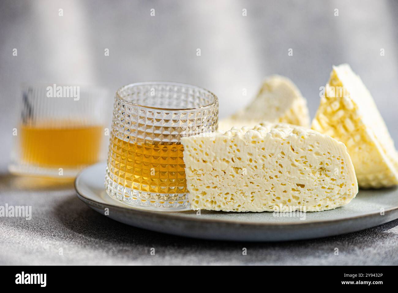 Fotografische Darstellung des traditionellen georgischen Sulguni-Käses zusammen mit einem Glas Bernstein, serviert auf einem Teller mit strukturiertem Hintergrund Stockfoto