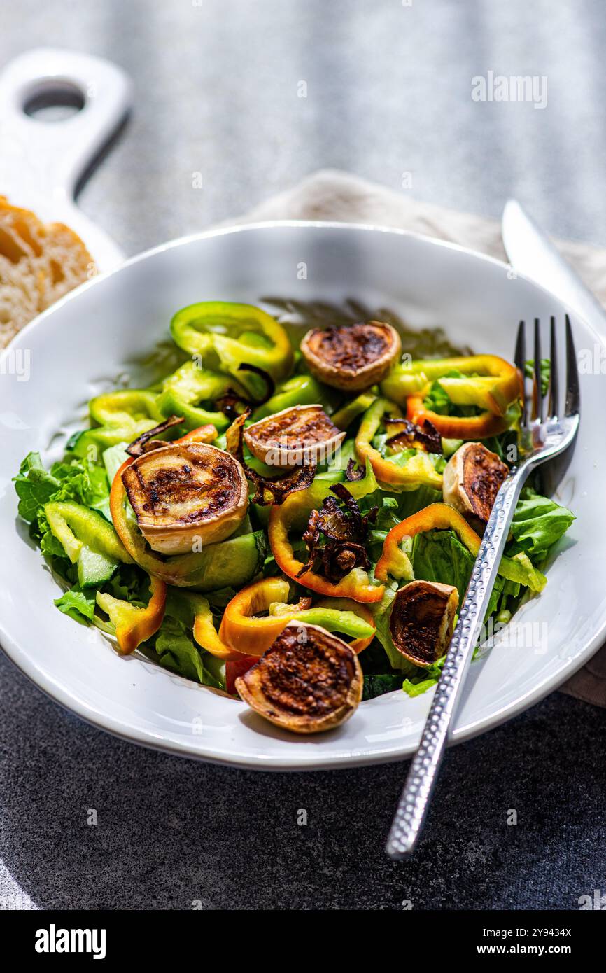 Ein gesunder heißer Salat mit gegrillten weißen Mini-Auberginen-Hälften, frisch geschnittenen grünen Paprika, knusprigen gebratenen Zwiebelringen und frischem Kopfsalat Stockfoto
