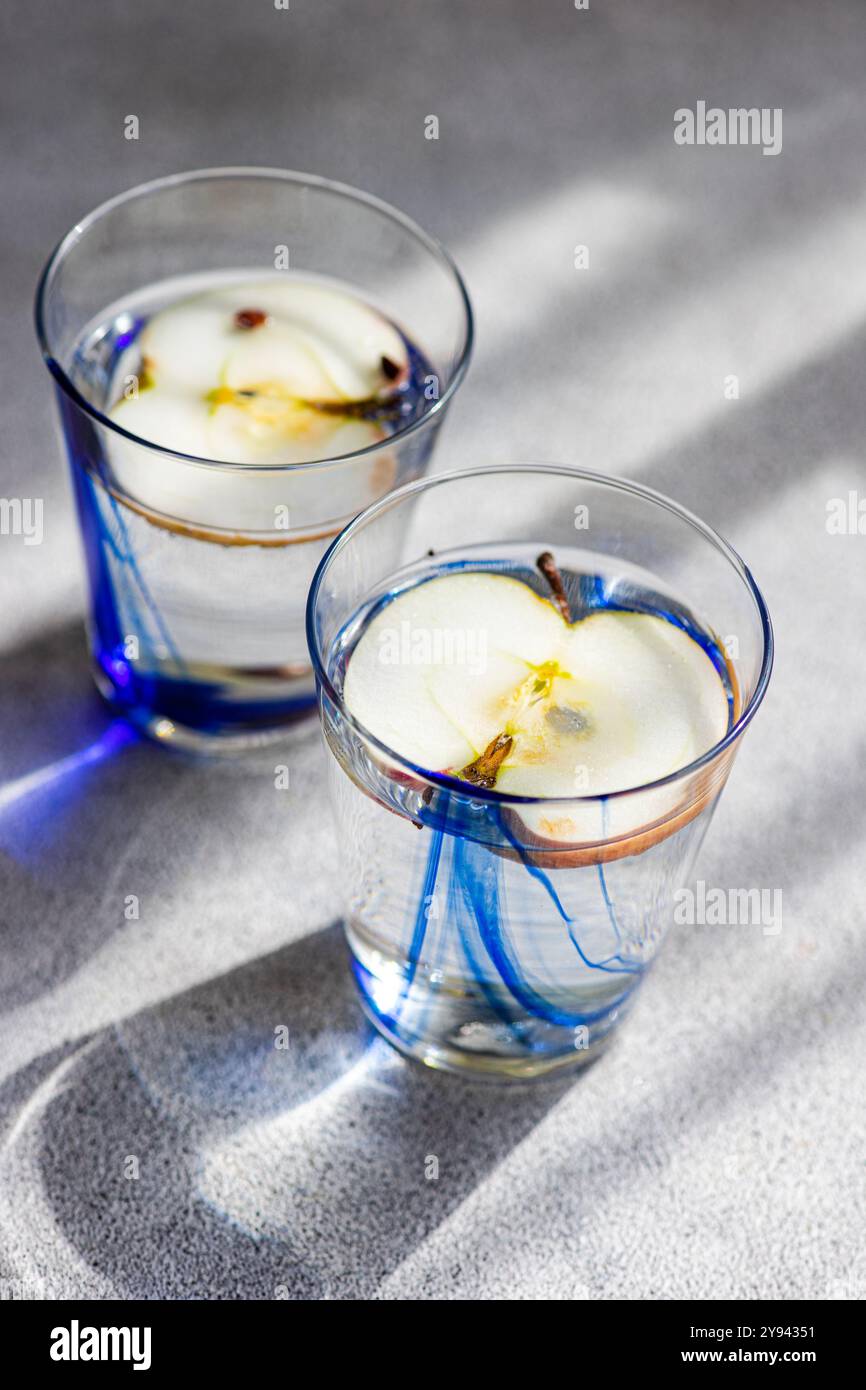 Von oben zwei Gläser Apfelwasser mit Scheiben Reifen Apfels und Bio-Apfelessig, präsentiert auf einer strukturierten Oberfläche mit Schatten. Stockfoto