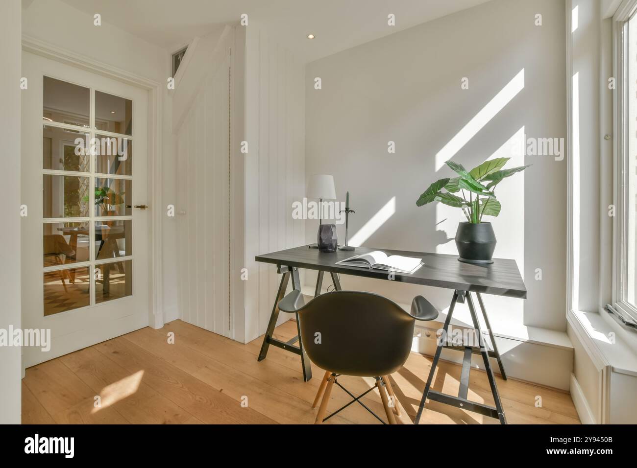 Ein gut beleuchteter, minimalistischer Home Office-Bereich mit einem eleganten Schreibtisch, modernem Stuhl und einer Topfpflanze. Stockfoto