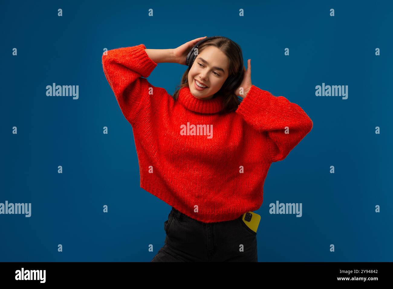 Emotional staunendes Mädchen, das Musik mit kabellosen Kopfhörern auf blauem Hintergrund hört Stockfoto