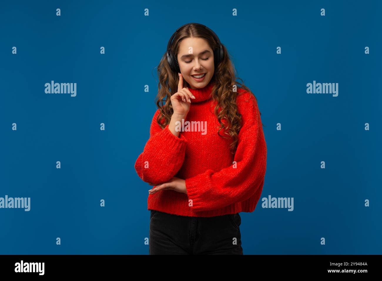 Emotional staunendes Mädchen, das Musik mit kabellosen Kopfhörern auf blauem Hintergrund hört Stockfoto