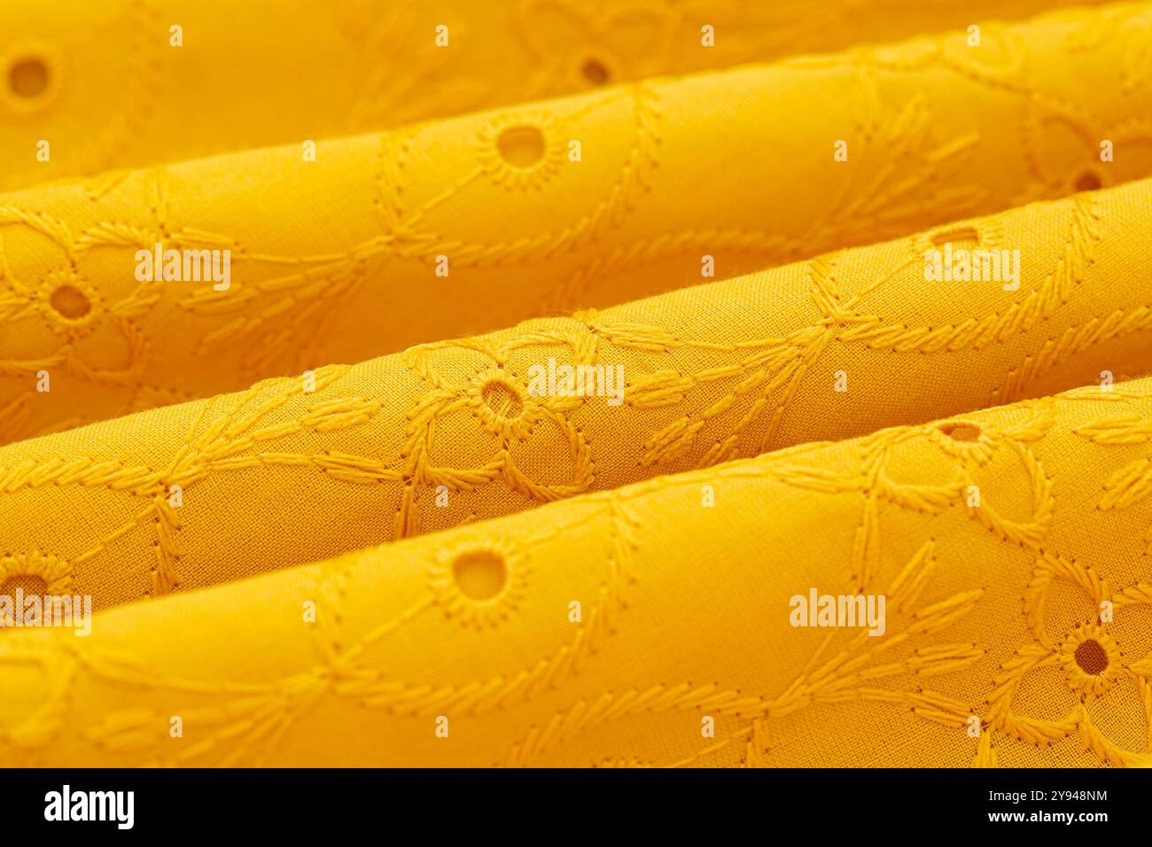 Nahaufnahme aus gelbem besticktem Stoff in Falten, der komplizierte Muster und Textur hervorhebt, perfekt für Mode- und Innenarchitekturprojekte Stockfoto