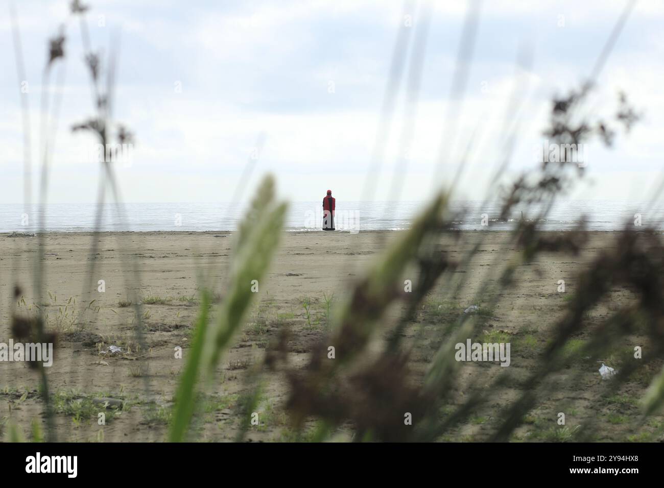 Einsame Frau in Rot, die die Weite des Meeres betrachtet. Gelassenheit, Frieden, Kontemplation. Stockfoto