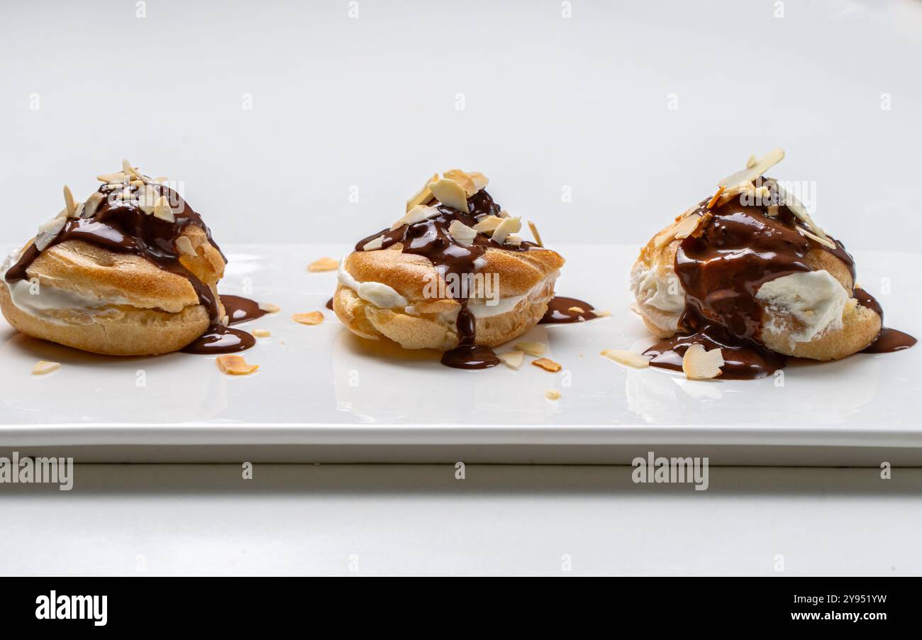 Profiteroles nach einem traditionellen französischen Rezept mit Vanillepudding, mit Schokolade getränkt und mit Mandelblättern auf weißem Hintergrund verziert. Hallo Stockfoto