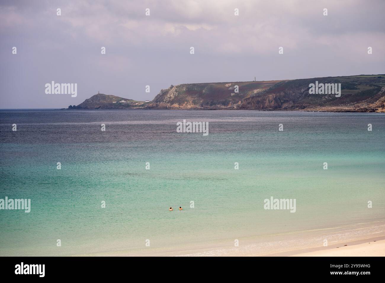 In der Sennen Cove in der Nähe von Land's End schwimmen die Menschen im Meer, mit der Landzunge Cape Cornwall in der Ferne. Stockfoto