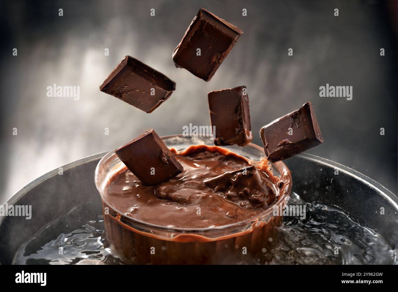 Schokoladenstücke fallen in eine Glasschale in einem Wasserbad zum Schmelzen, Kopierraum, ausgewählter Fokus, geringe Schärfentiefe Stockfoto