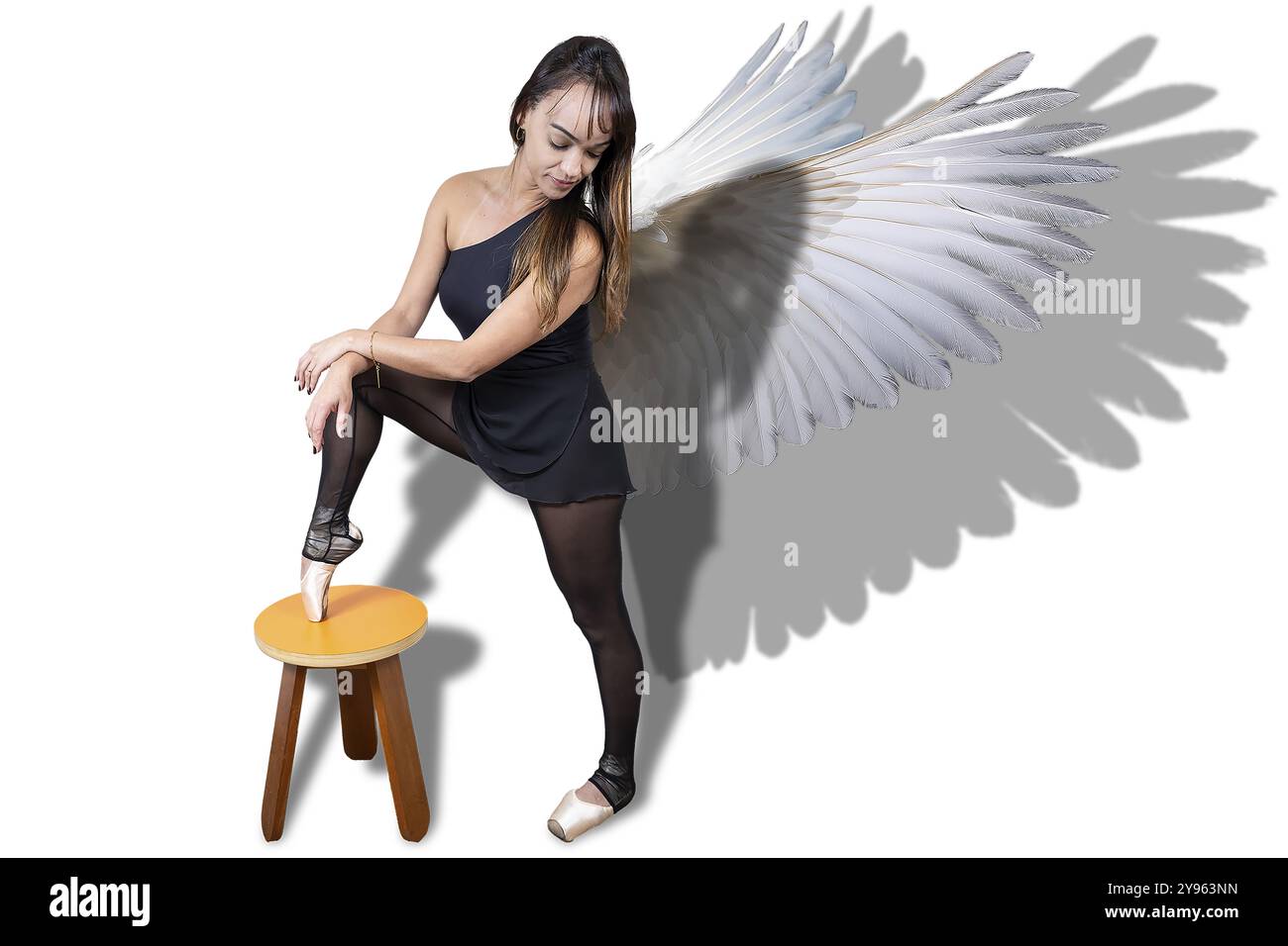 37 Jahre alte brasilianische Ballerina posiert mit weißen Flügeln mit dem Fuß auf einer Holzbank mit Schatten 7. Stockfoto