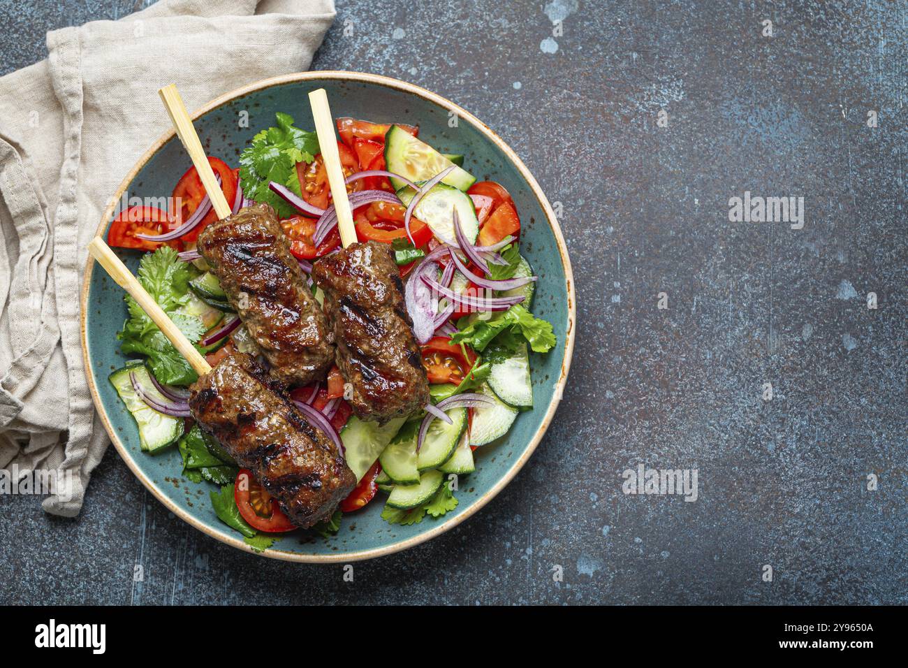 Gegrilltes Spießfleisch Rindfleisch Kebabs auf Stäbchen serviert mit frischem Gemüsesalat auf Teller auf rustikalem Betonhintergrund von oben. Traditionelles Mittleres Eas Stockfoto