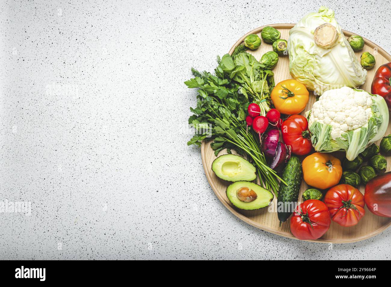 Rustikales Holztablett mit einer Auswahl an frischem Gemüse und Grün auf weißem Küchentisch. Vegetarische oder diätetische Lebensmittel aus ökologischen Zutaten, Stockfoto