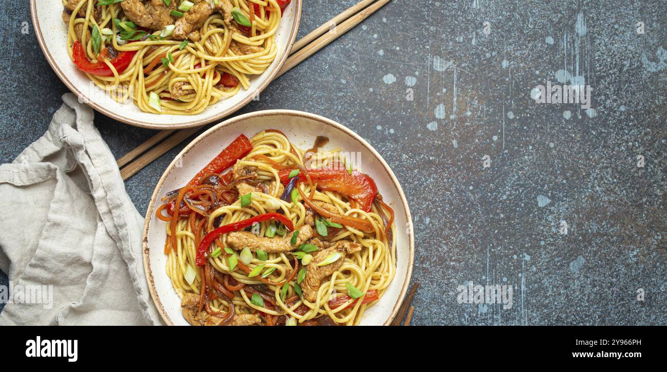 Zwei Schüsseln mit Chow mein oder Lo mein, traditionellen chinesischen Pfannennudeln mit Fleisch und Gemüse, serviert mit Essstäbchen von oben auf rustikalem blauen Coffee Stockfoto