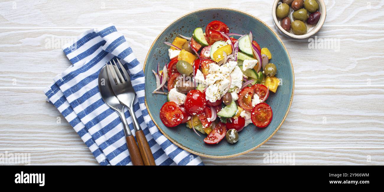 Griechischer frischer, gesunder, farbenfroher Salat mit Fetakäse, Gemüse, Oliven in blauer Keramikschüssel auf rustikalem weißem Holzhintergrund mit Blick von oben, mediterrane Küche Stockfoto