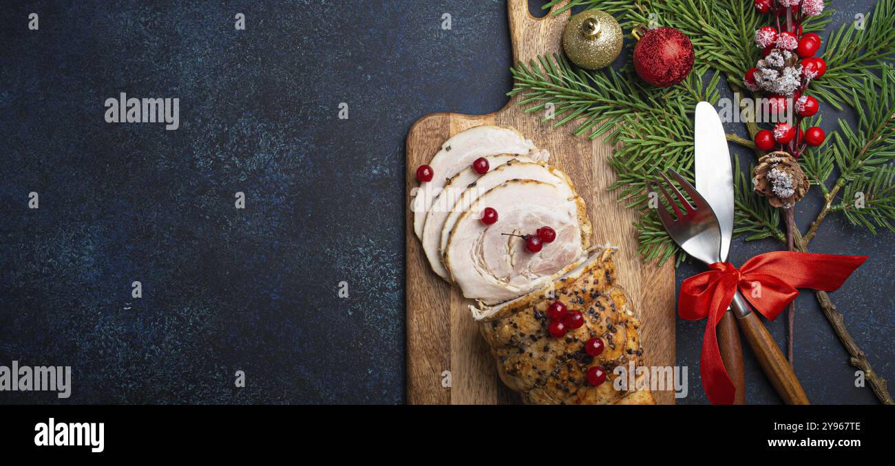 Weihnachtlich gebackener Schinken in Scheiben mit roten Beeren und festliche Dekorationen auf Holzschneidplatten, dunkler rustikaler Hintergrund von oben. Weihnachten und Neujahr Stockfoto