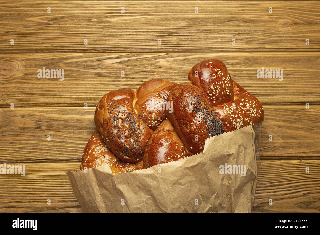 Frisch gebackenes Challah-Brot, bedeckt mit Mohn und Sesamsamen in einer Papiertüte, Blick von oben auf rustikalen hölzernen Hintergrund, traditionelle festliche jüdische Küche Stockfoto