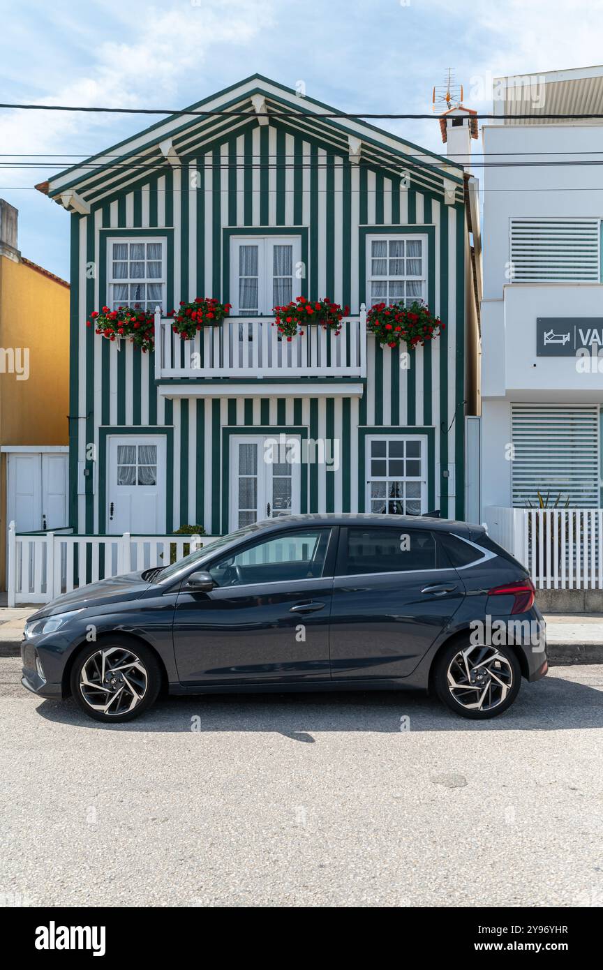 Costa Nova, Portugal - 11. September 2024 : Ein modernes Auto parkt neben einem charmanten gestreiften Haus mit Blumen. Stockfoto