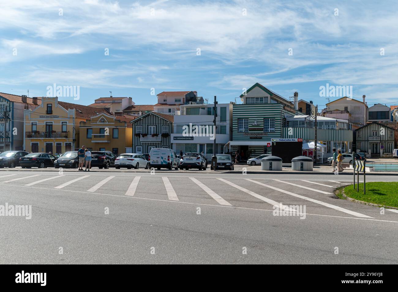 Costa Nova, Portugal - 11. September 2024 : Besucher schlendern in der Nähe von geparkten Autos in einer bezaubernden Küstenstadt unter blauem Himmel. Stockfoto