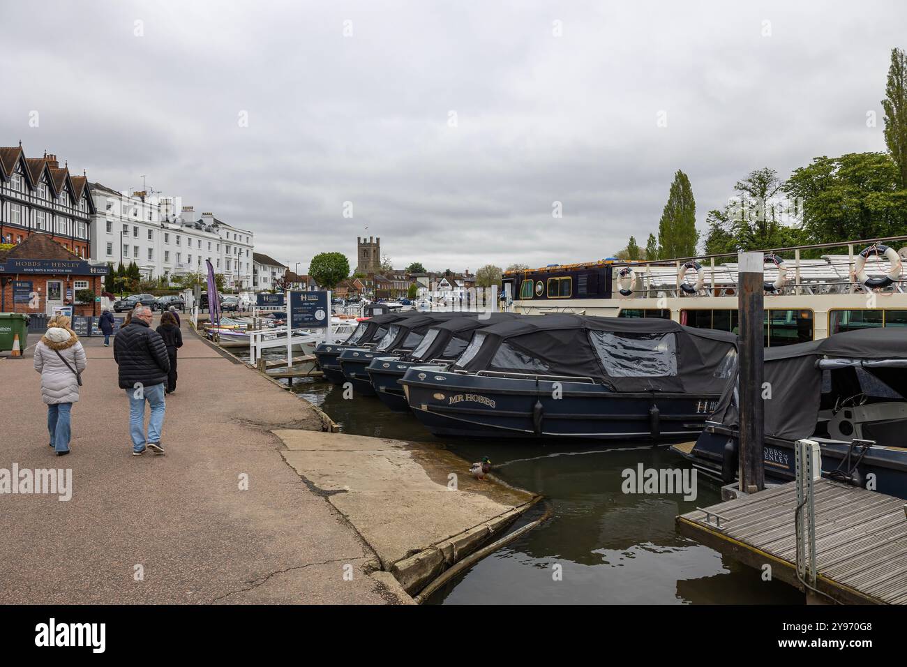 Ein Paar mittleren Alters läuft am Grey Day in Richtung Henley Promenade mit angelegten Booten auf der Themse Stockfoto