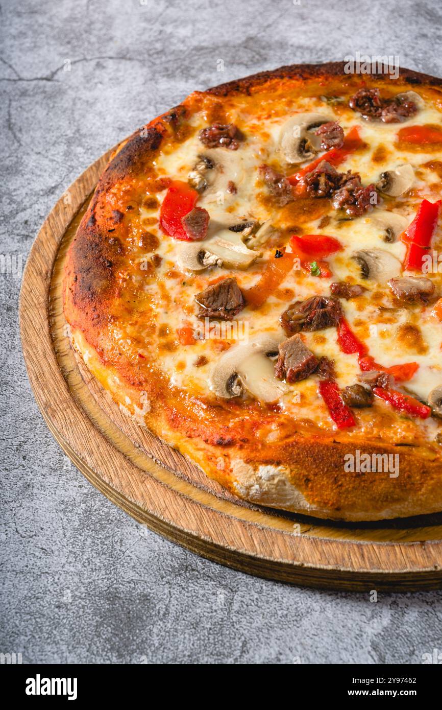Pizza mit Paprika und Roastbeef auf dem Schneidebrett auf einem Steintisch Stockfoto