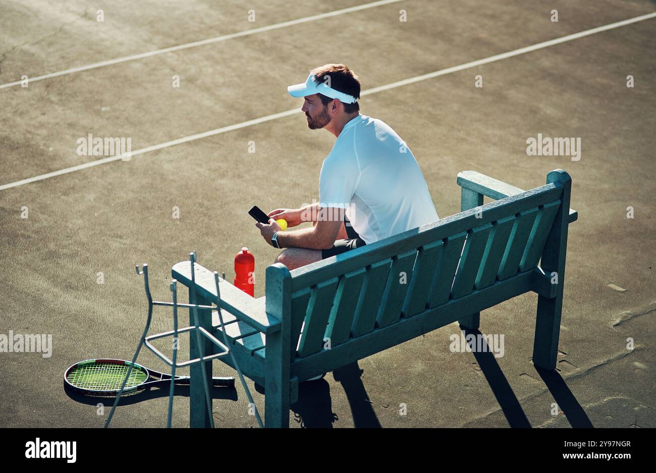 Tennisplatz, Sport und Mann auf der Bank mit Smartphone beim Training oder Trainingspause in sozialen Medien. Männlicher Mensch, draußen und entspannen Sie sich beim Nachdenken Stockfoto