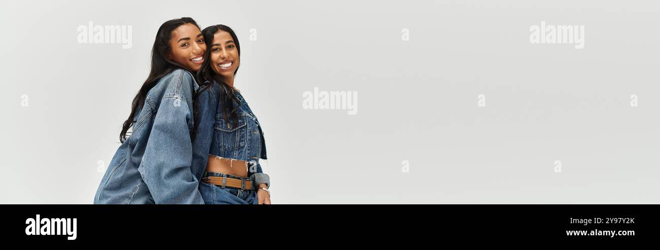 Zwei modische junge Frauen posieren gemeinsam in stylischen Denim-Outfits und versprühen Freude. Stockfoto