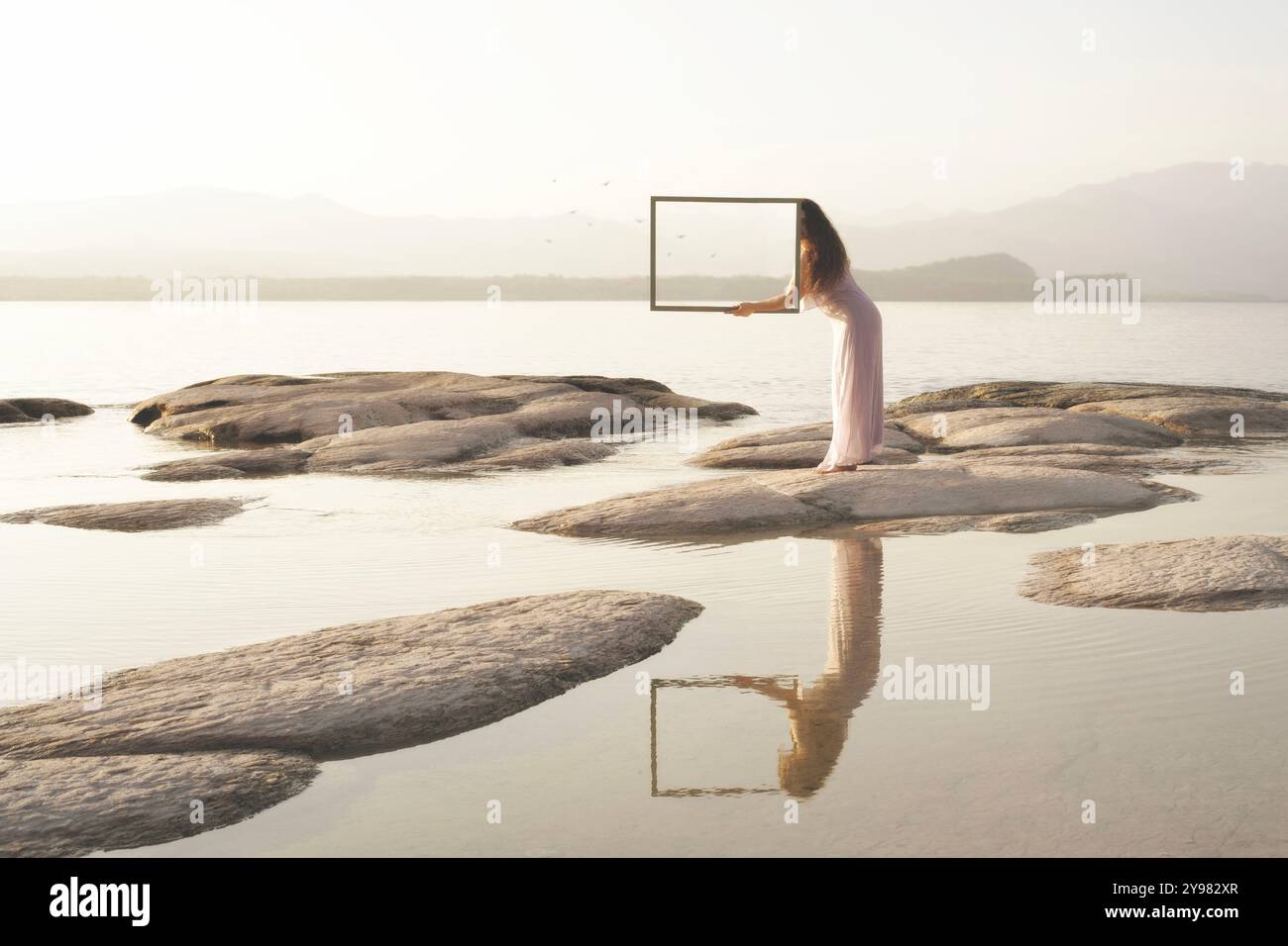 Die Frau versteckt sich hinter einem magischen Spiegel, der das Meer widerspiegelt, das Konzept der Freiheit Stockfoto