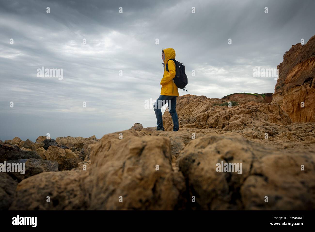 Frau mit gelber Jacke, die allein über felsige Berghänge geht und die Aussicht betrachtet Stockfoto