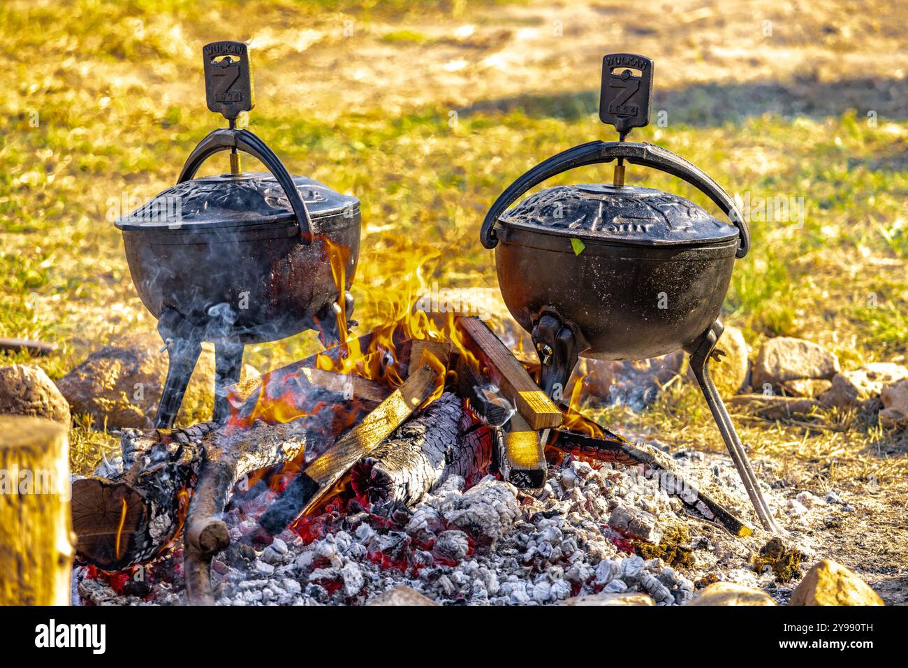 Zwei große schwarze gusseiserne Töpfe, die bei einer hohen Temperatur des Feuers auf dem Gras platziert wurden, um eine Mahlzeit zuzubereiten, Artofli-Braten Stockfoto