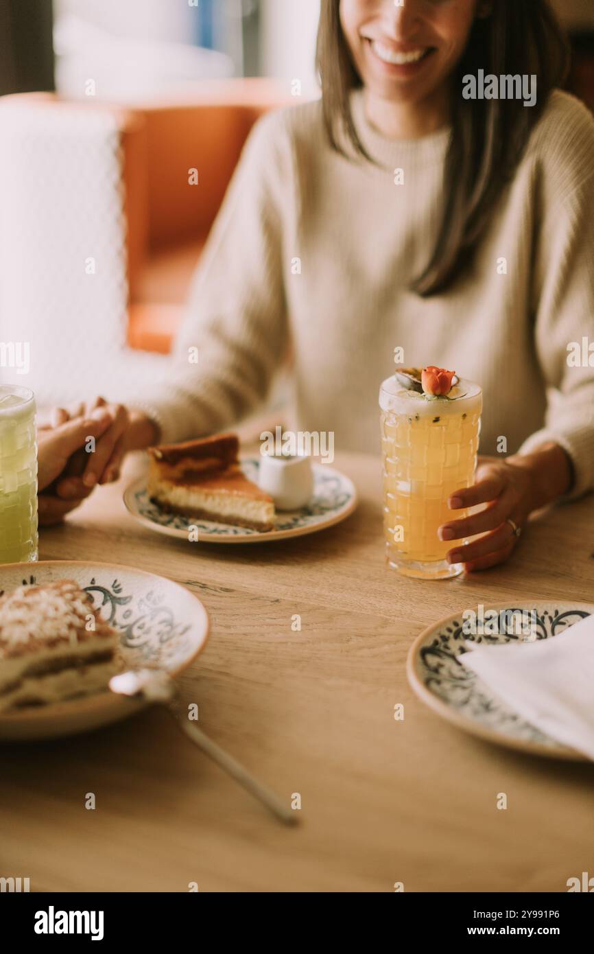 Eine Frau lächelt, während sie ein buntes Getränk hält, umgeben von köstlichem Essen. Freunde teilen Lachen und gemütliche Momente in einem charmanten Café während einer Leisu Stockfoto