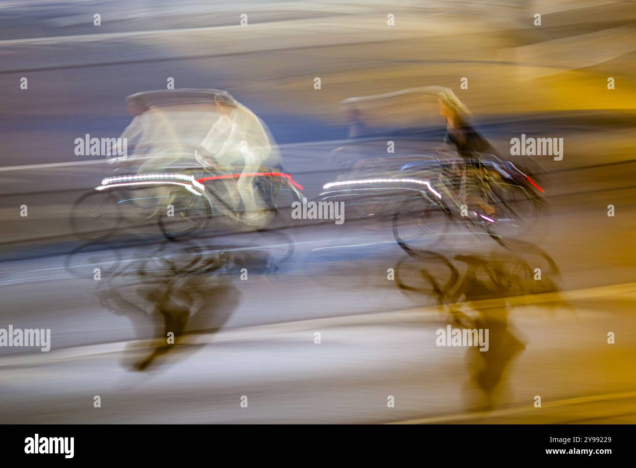 Dynamische Schwenkaufnahme für Radfahrer mit Bewegungsunschärfe auf den Straßen der Stadt bei Nacht. Lebendige Lichter und dynamische Bewegungen sorgen für ein rasantes urbanes Leben. Stockfoto