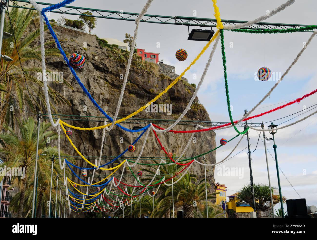 Farbenfrohe Festivaldekorationen hängen in ponta do sol vor dem Hintergrund der Klippen und Palmen in der Luft Stockfoto