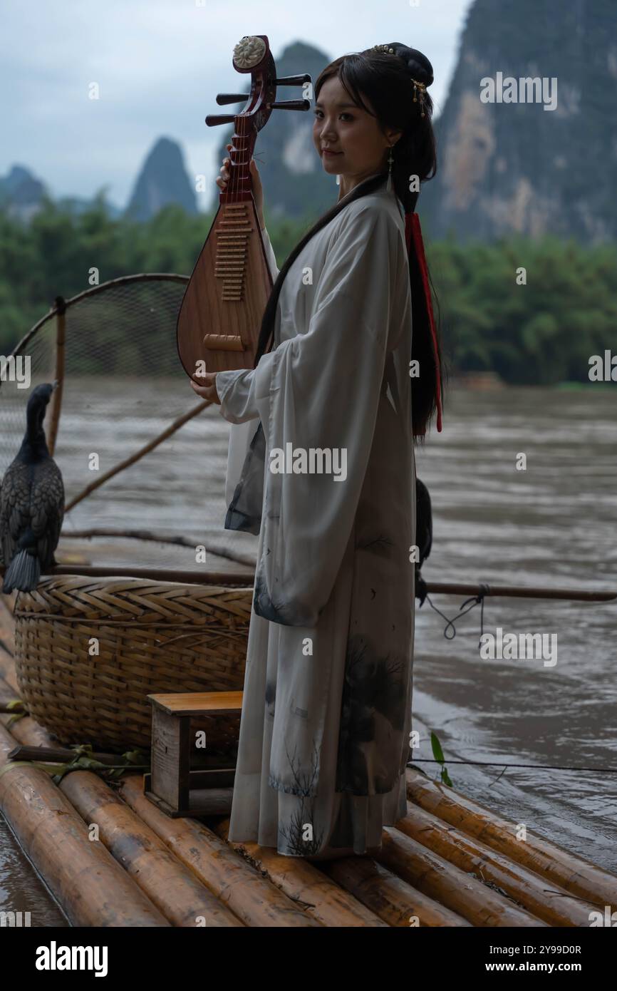 Eine junge Frau in Hanfu spielt Pipa auf einem Bambusfloß. Xingping, China. Vertikale Aufnahmen Stockfoto