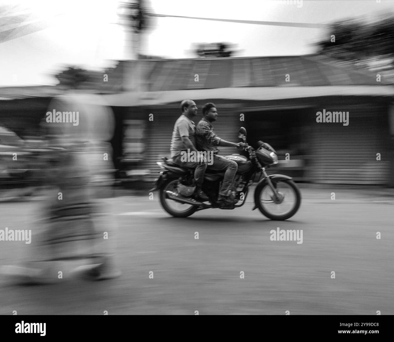 Verschwommene Bewegung eines Motorrads mit zwei Fahrern, die durch eine geschäftige Straße in Bangladesch fahren. Schwarzweiß-Bewegungsunschärfen. Stockfoto