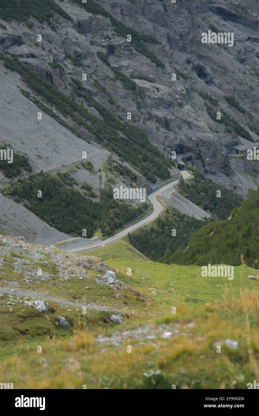 Malerische Bergstraße schlängelt sich durch das zerklüftete Gelände des Stilfserjochs in Italien, mit scharfen Kurven und Tunneln, die in den Berghang gehauen wurden. Stockfoto