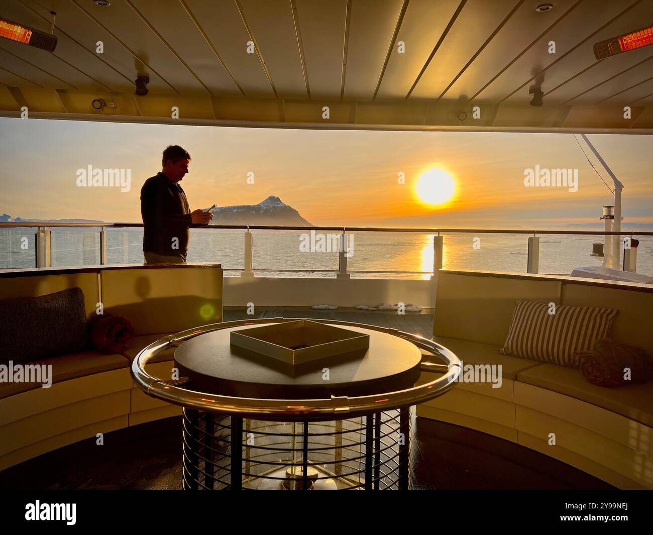 An Bord des Kreuzfahrtschiffs Lindblad Nat Geo in der Antarktis genießt ein Passagier den atemberaubenden Sonnenuntergang über dem südlichen Ozean mit Blick auf eine Insel Stockfoto