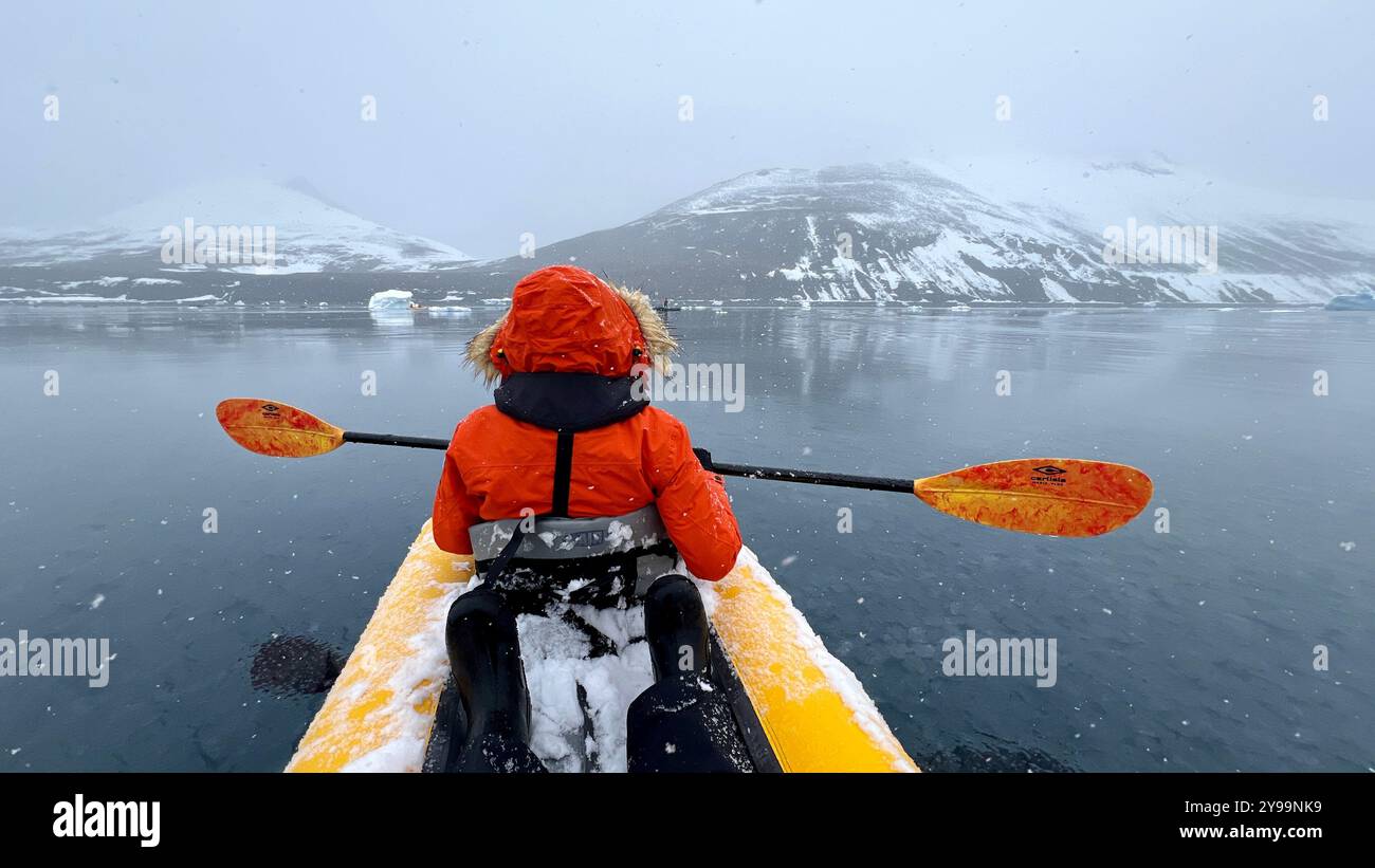 Ein Passagier von der Nat Geo Endurance Kajak durch ruhige, eiskalte Gewässer in der Nähe der Trinity Peninsula in der Antarktis, umgeben von schneebedeckten Bergen Stockfoto