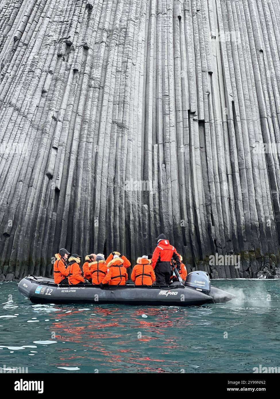 Touristen in orangefarbenen Jacken erkunden die gewaltigen geologischen Formationen des Edinburgh Rock, der sich auf den abgelegenen South Shetland Islands in der Antarktis befindet Stockfoto