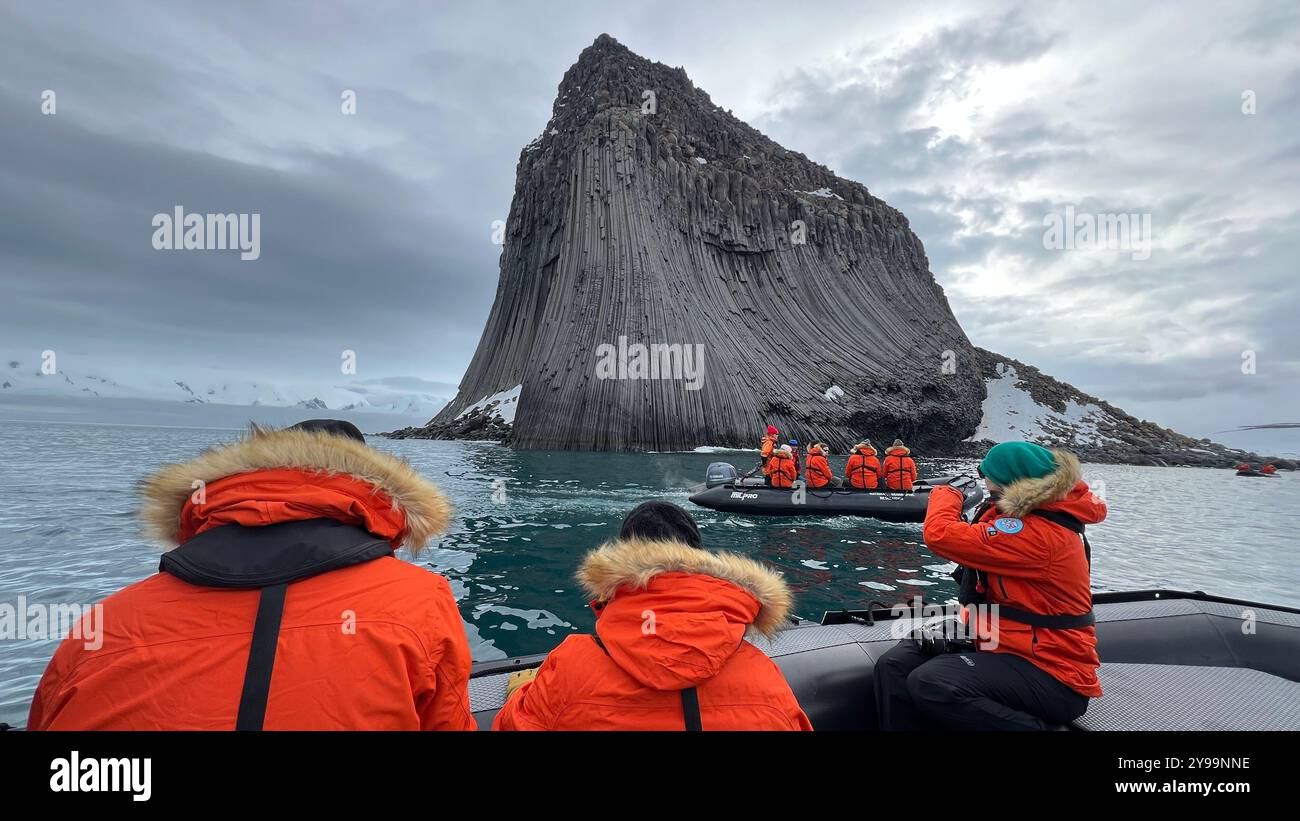 Touristen in orangefarbenen Jacken erkunden die gewaltigen geologischen Formationen des Edinburgh Rock, der sich auf den abgelegenen South Shetland Islands in der Antarktis befindet Stockfoto