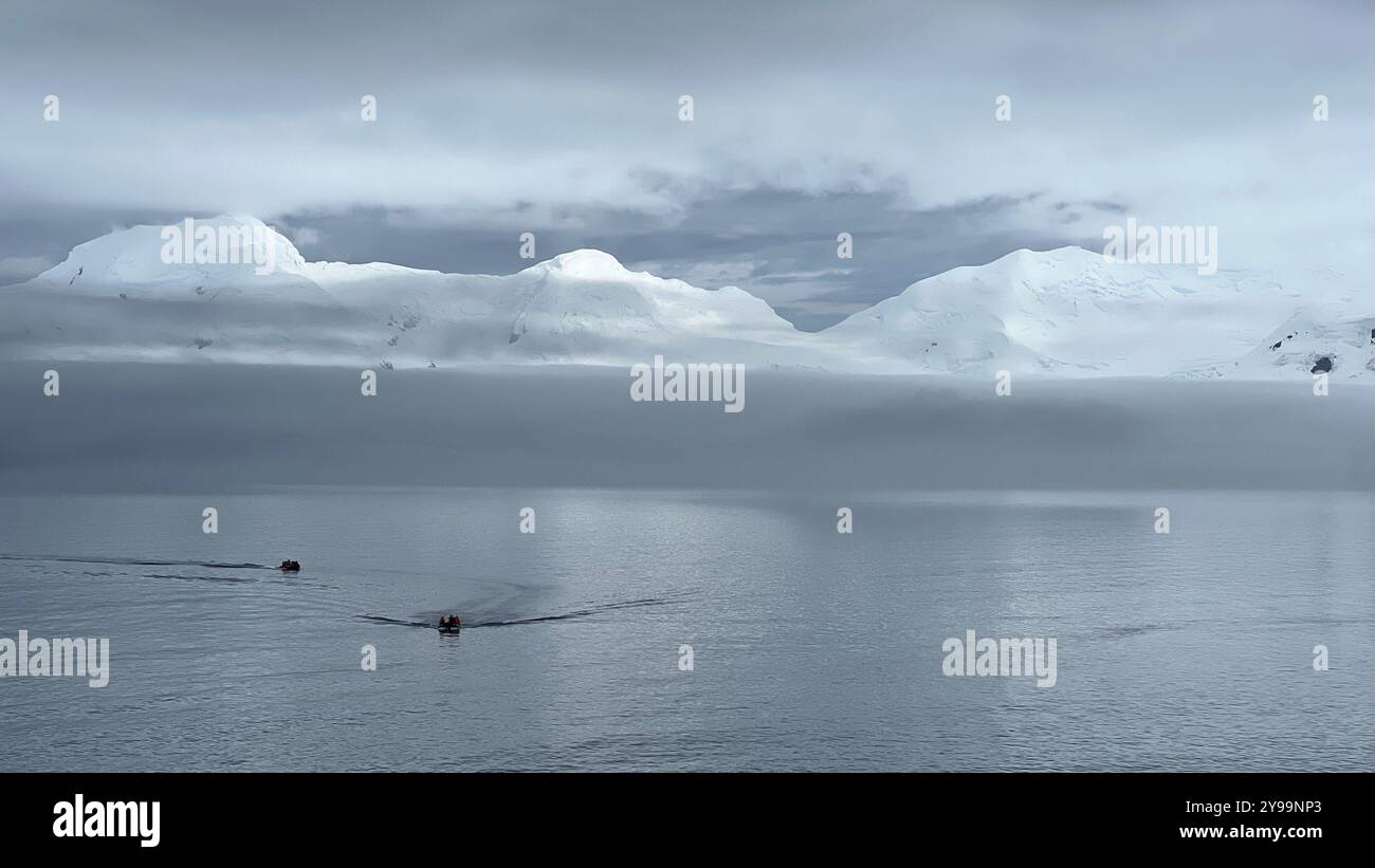 Zwei kleine Expeditionsboote fahren in Richtung der schneebedeckten Berge der Antarktis und gleiten durch die ruhigen Gewässer des Südlichen Ozeans - Smartphone-aufgenommenes Stockfoto