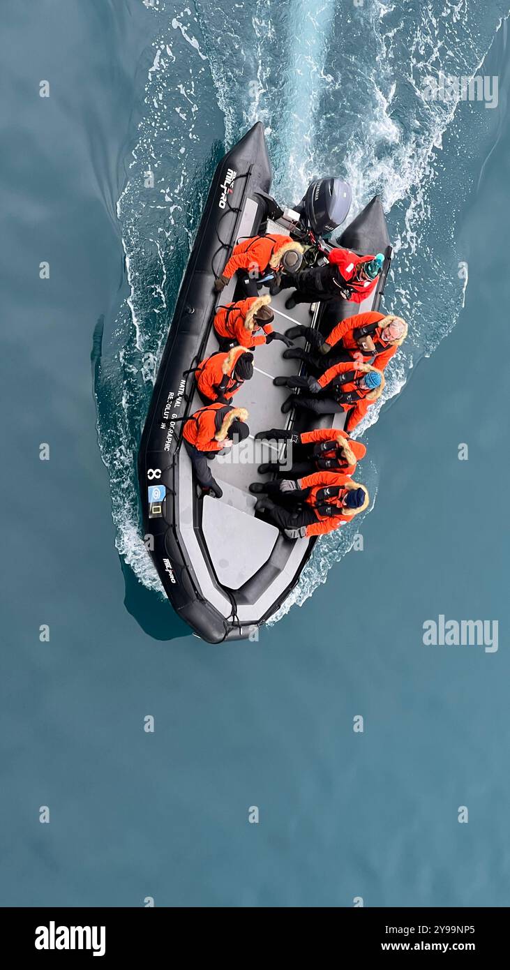 Ein Blick von oben auf ein kleines Expeditionsboot, das Passagiere in leuchtend orangefarbenen Jacken befördert, während sie die Gewässer der Antarktis erkunden Stockfoto