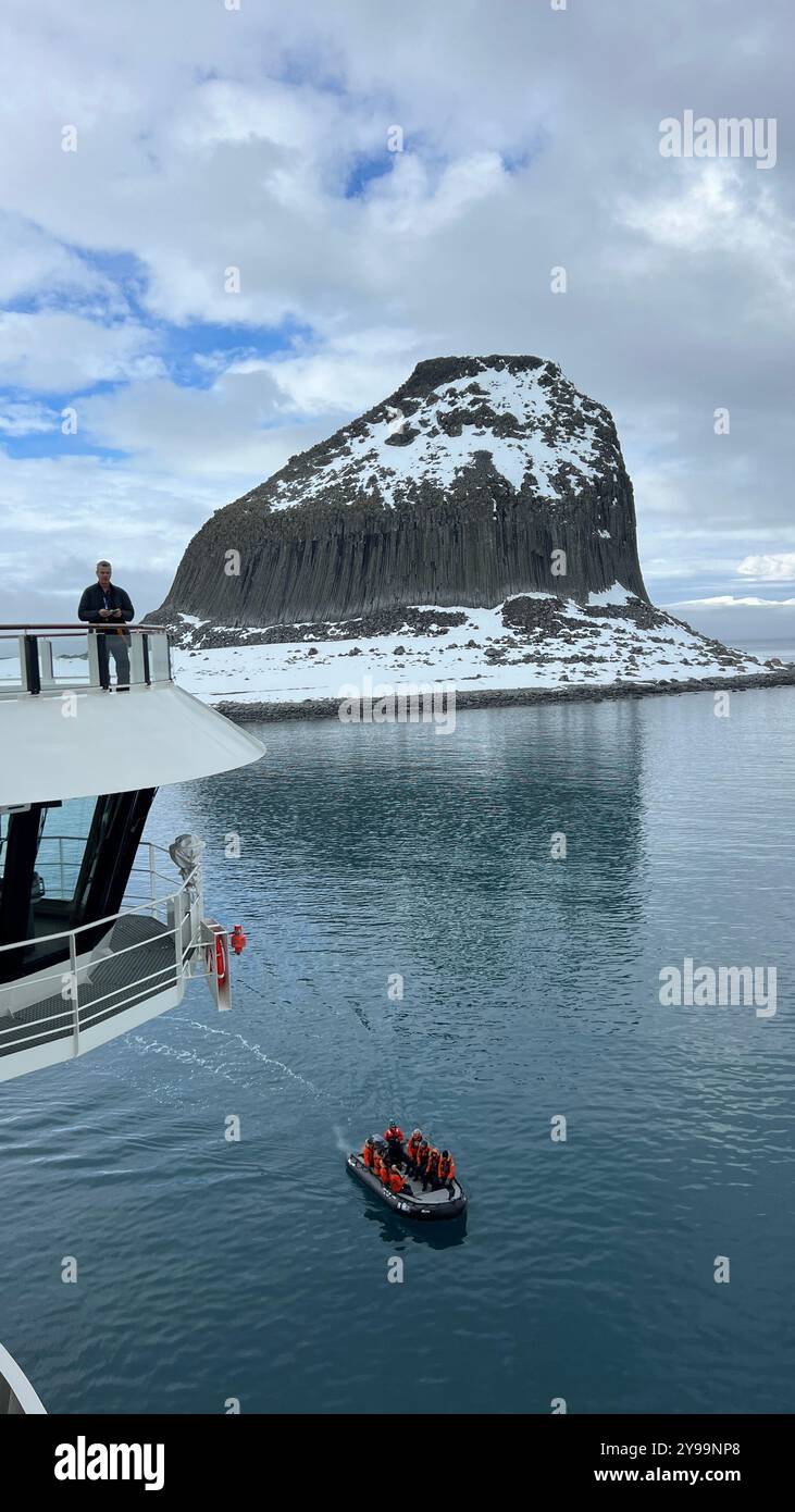 Passagiere an Bord der Lindblad Nat Geo Endurance beobachten ein kleines Expeditionsboot, das durch die ruhigen Gewässer in der Nähe des Edinburgh Rock in der Antarktis fährt Stockfoto