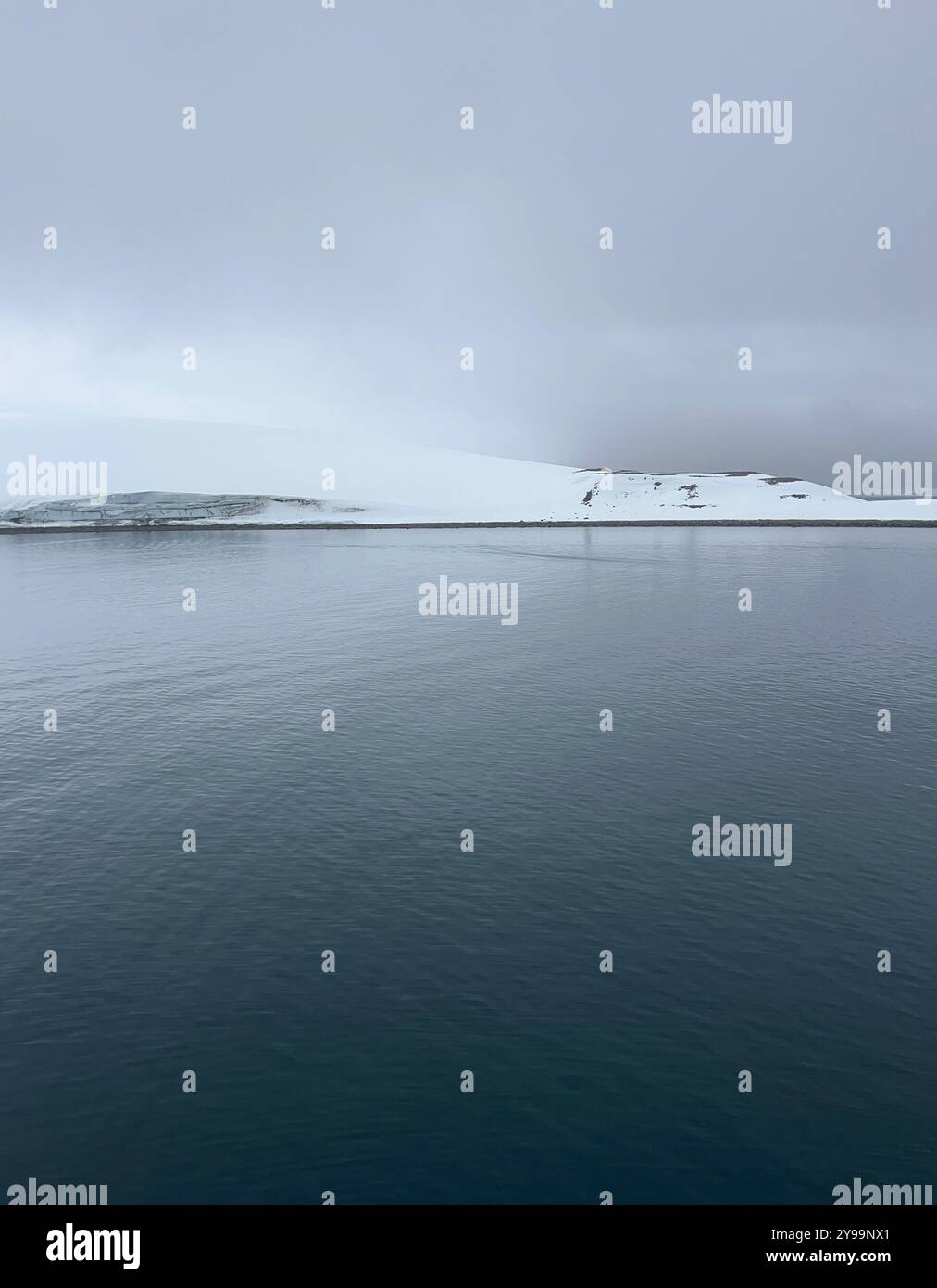 Ein ruhiger Blick auf den südlichen Ozean in der Antarktis, mit glattem Wasser, das den bewölkten Himmel und die schneebedeckte Landschaft reflektiert Stockfoto