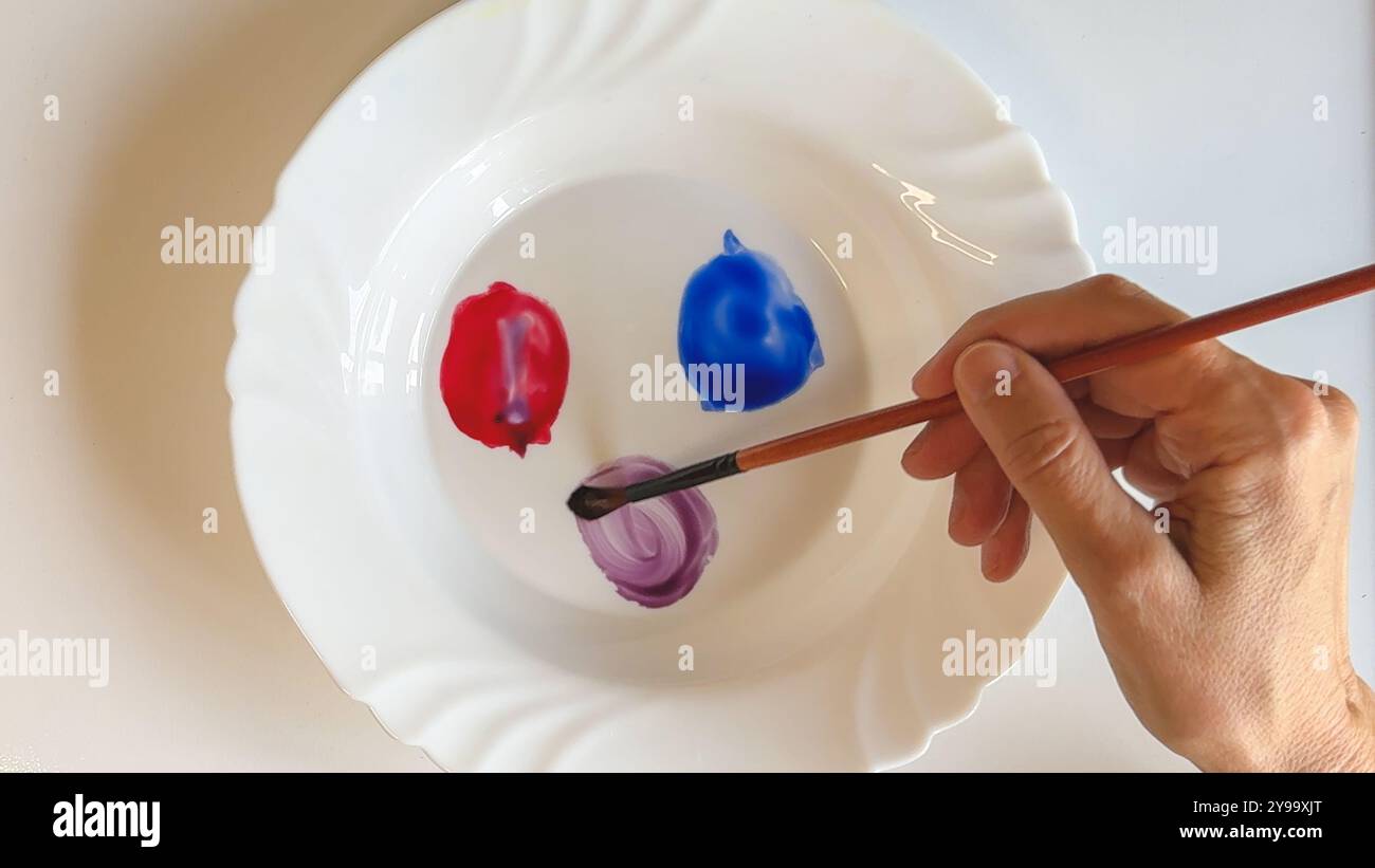 Mischen von violettem Aquarell auf einer Platte mit roten und blauen Farben, Nahansicht Stockfoto