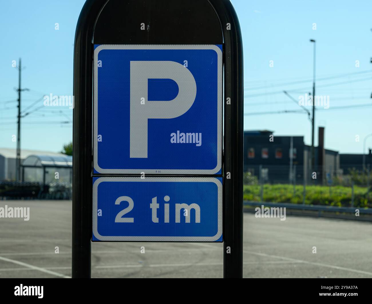 Ein blaues Parkschild zeigt ein „P“-Symbol mit einer Zeitbegrenzung von zwei Stunden darunter vor dem Hintergrund eines städtischen Gebiets unter klarem blauem Himmel Stockfoto
