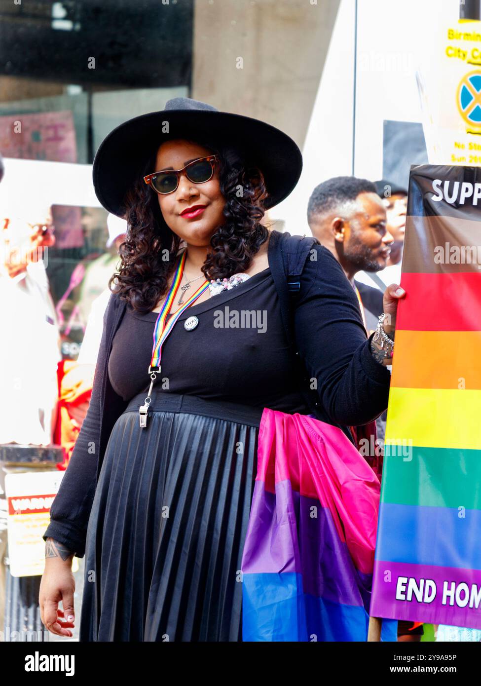 Lächelnde Frau im Pride Birmingham mit schwarzem Hut und Sonnenbrille und einer Regenbogenfahne Stockfoto