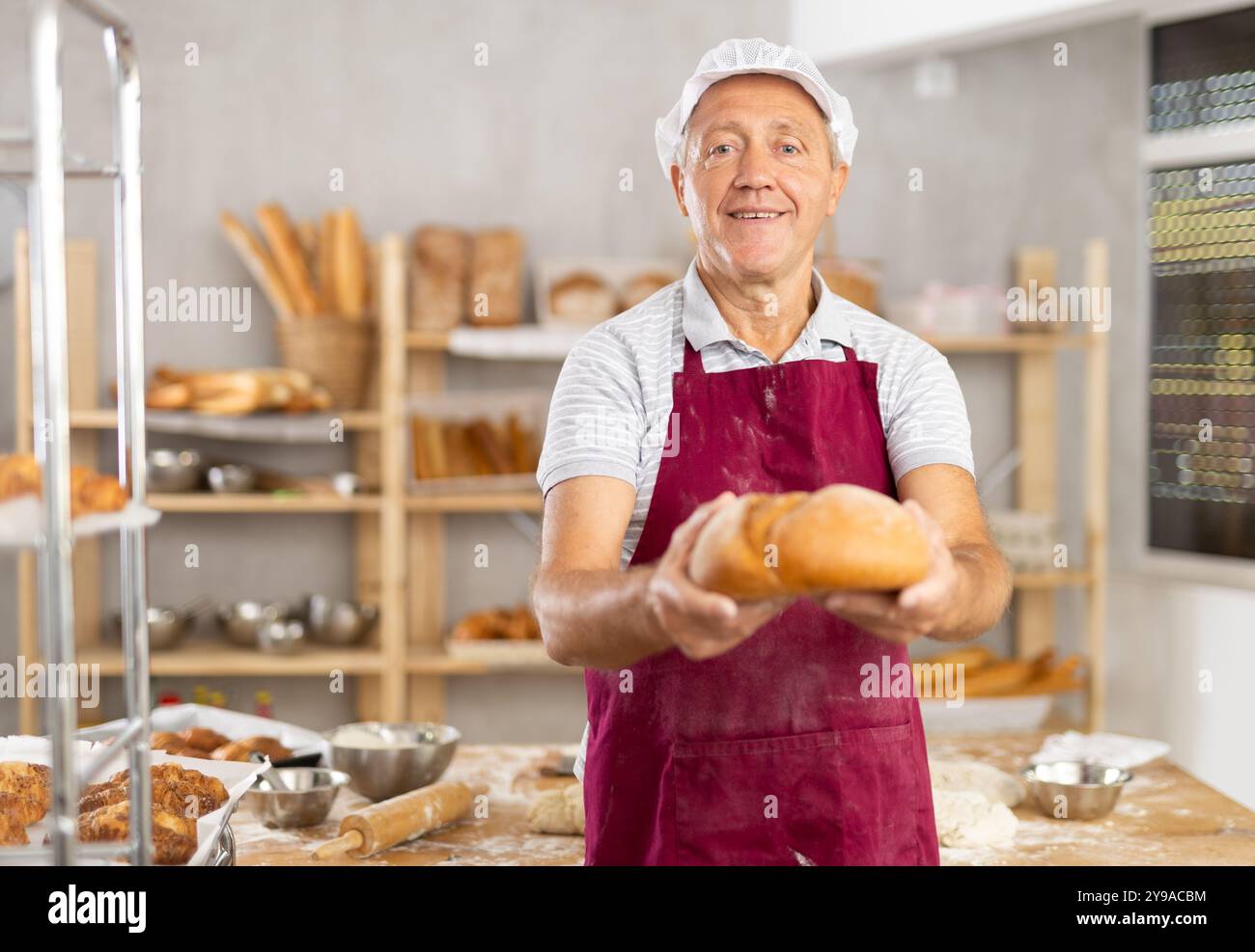 Lächelnder älterer Bäcker, der goldene Brotlaibe in der Bäckerei hält Stockfoto