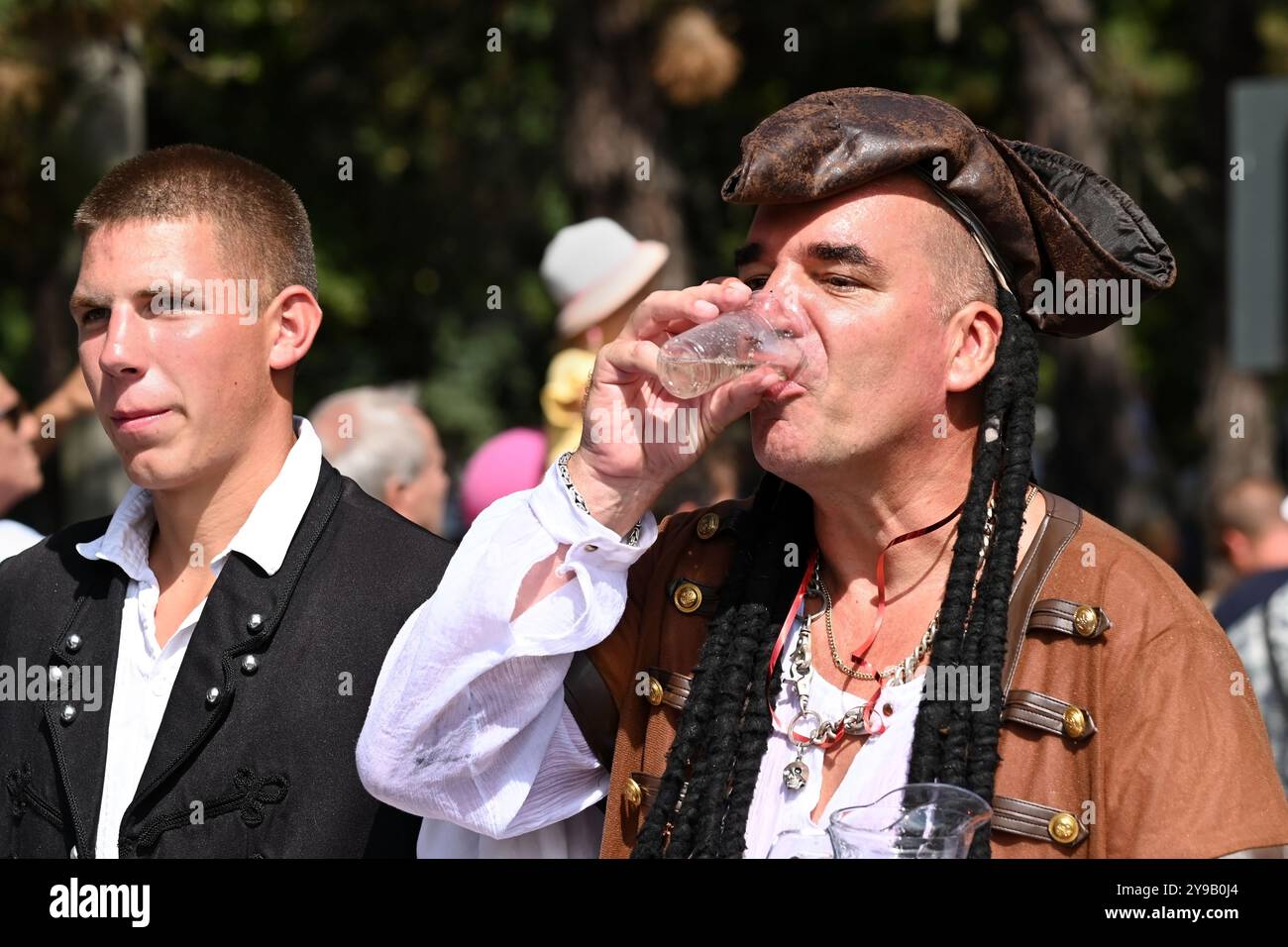 Badacsony, Balaton, Ungarn - 8. September 2024: Straßenparade des Weinerntefestes, zwei Männer in traditioneller und ausgefallener Kleidung trinken Wein Stockfoto Badacsony, Balaton, Ungarn - 8. September 2024: Straßenparade des Weinerntefestes, zwei Männer in traditioneller und ausgefallener Kleidung trinken Wein Stockfoto