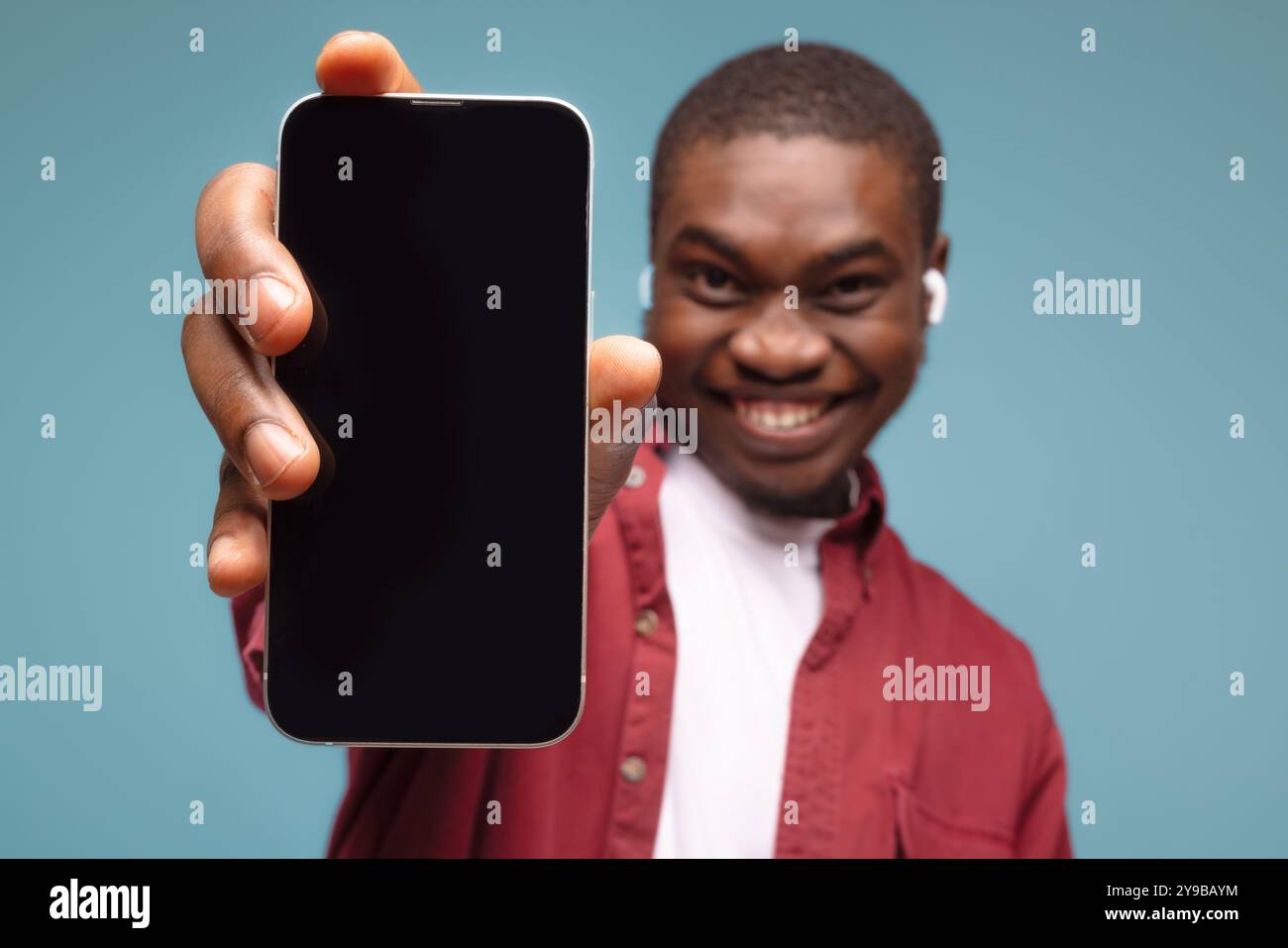 Mobile Werbung. Überglückter schwarzer Mann, der auf Handy mit leerem weißen Bildschirm auf blauem Studiohintergrund zeigt, Modell für App oder Website. Cellphon Stockfoto