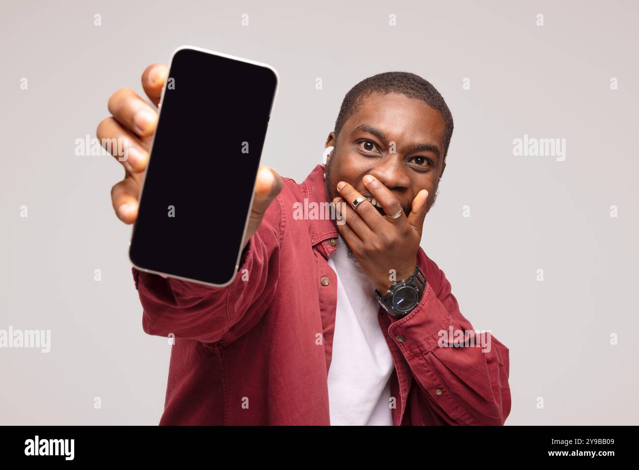 Überraschter afrikanischer junger Mann, der Smartphone zeigt und sich über den Erfolg freut, auf weißem Hintergrund. Stockfoto