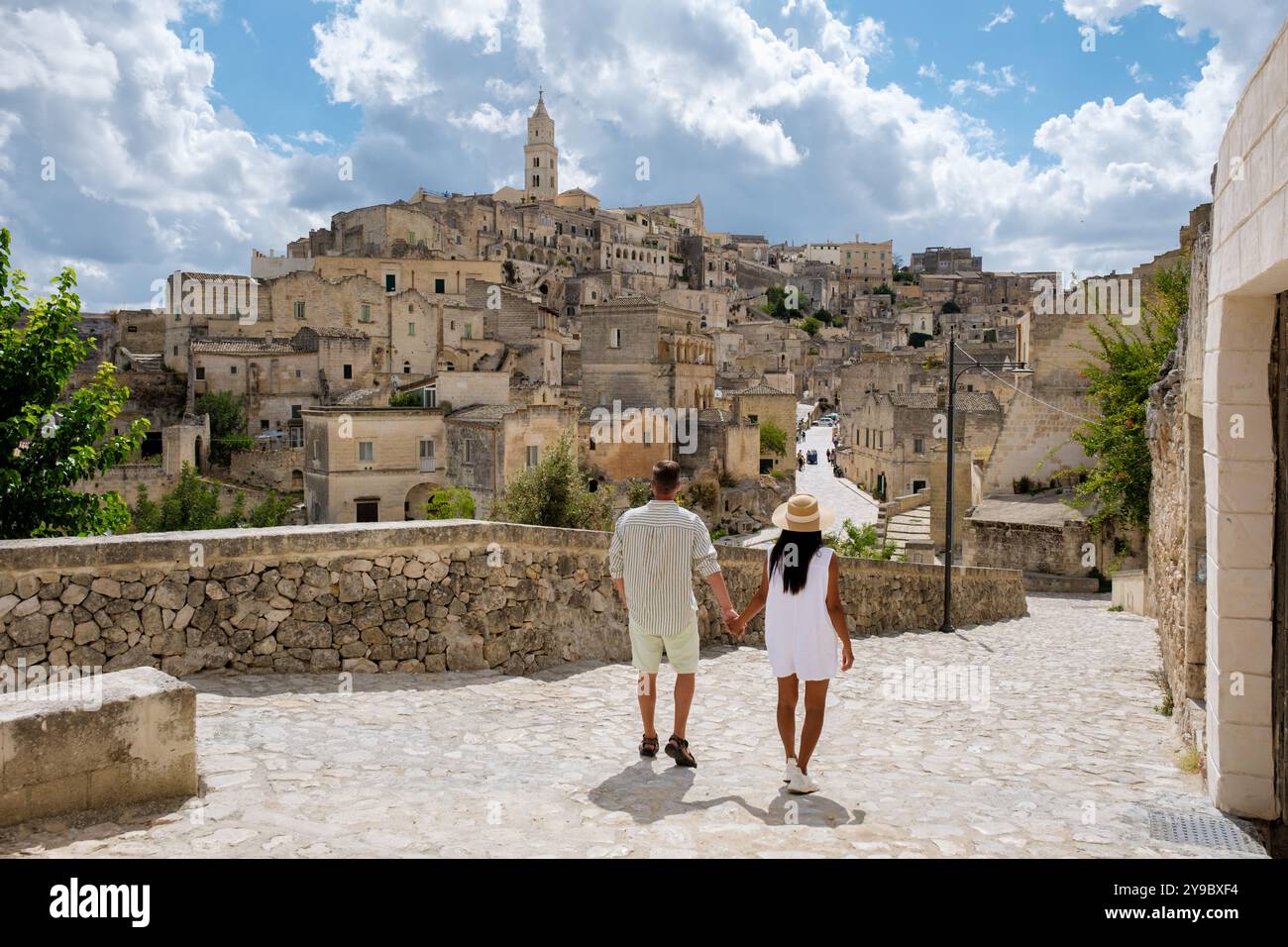 Zwei Liebhaber schlendern Hand in Hand auf kopfsteingepflasterten Pfaden, umgeben vom historischen Charme von Matera Italy, der atemberaubenden Architektur vor einer hellen Wolke Stockfoto